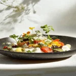 Try Terra Massoud's Mouthwatering Recipe Today 3 A beautifully plated dish featuring vibrant colors and fresh ingredients, such as herbs, spices, and a protein-rich main component. Garnished with edible flowers and a drizzle of sauce, the dish reflects a fusion of flavors and artistic presentation.